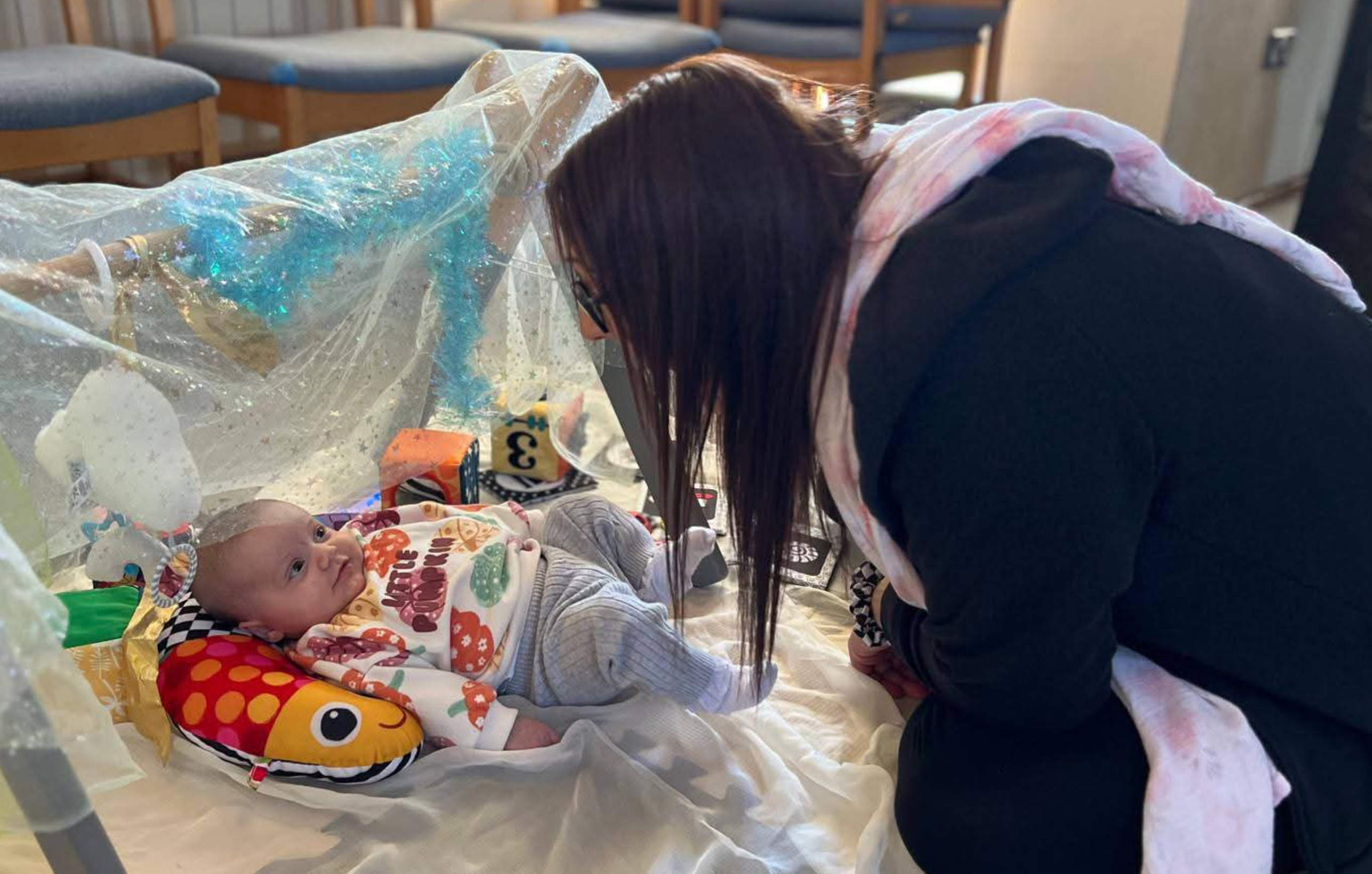 Child led on a bbaby bouncer staring up happily at mum